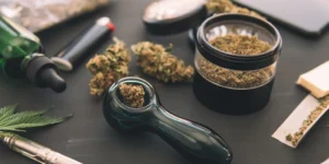 A dark but well lit table covered in cannabis flower and weed smoking accessories.