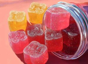 a round glass container overflowing with colorful cannabis gummies.