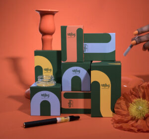 Several MFNY product boxes sitting on an orange surface and background with a vape pen and concentrate included.
